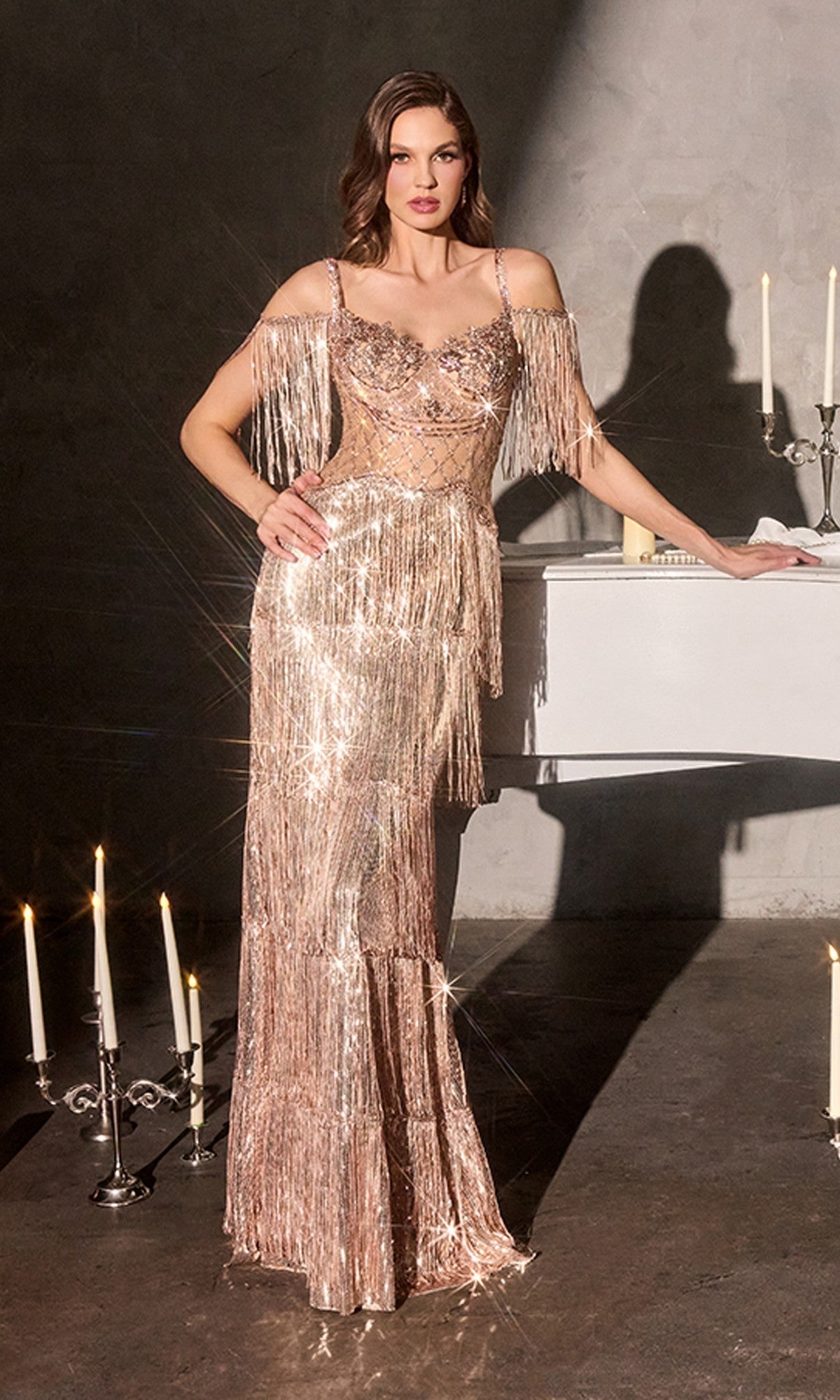 A woman in the Ladivine CDS563 Long Prom Dress in rose gold, featuring shimmering sequins and fringe, stands beside a white piano with candles in the background.